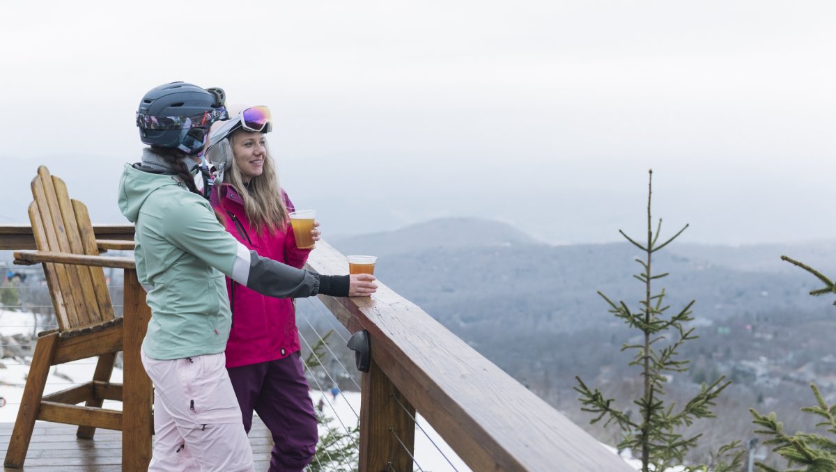 Two friends drinking beers on bar deck overlooking mountains and ski slopes