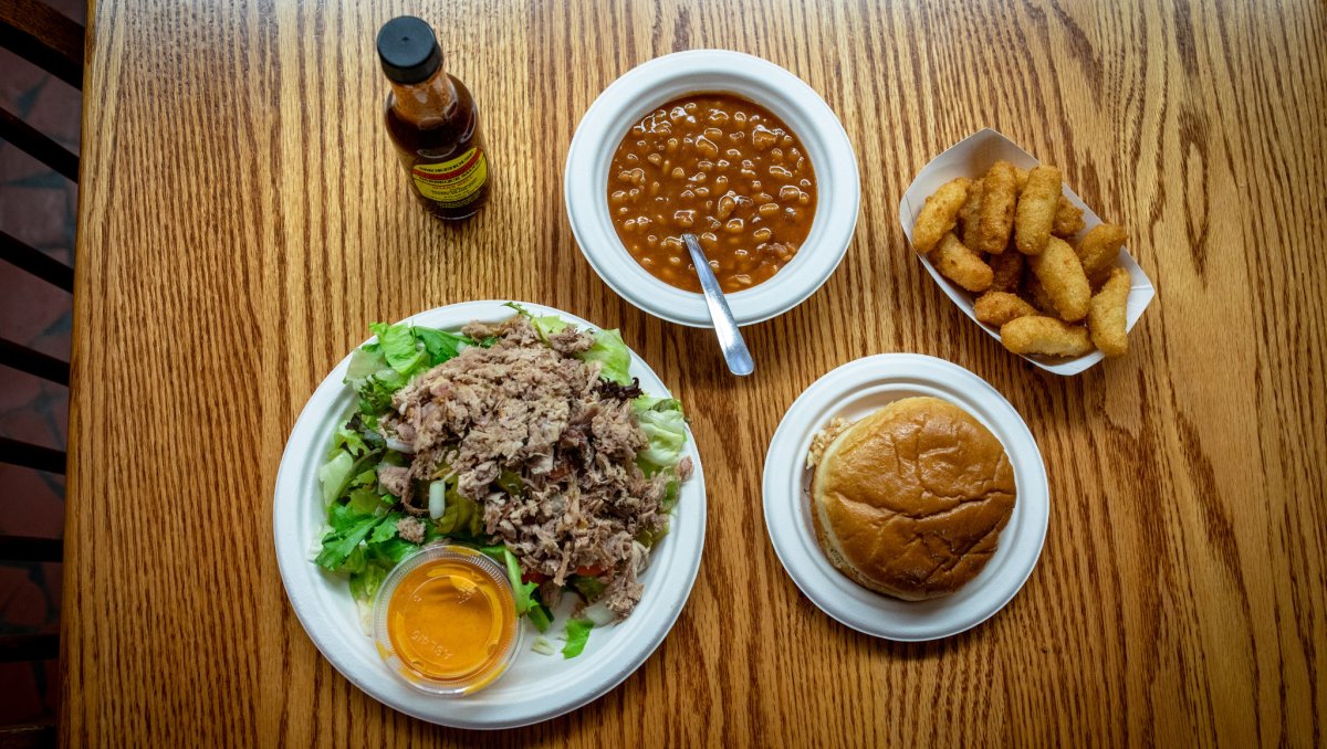 BBQ, baked beans, bread, hush puppies and sauce sitting on a wood table