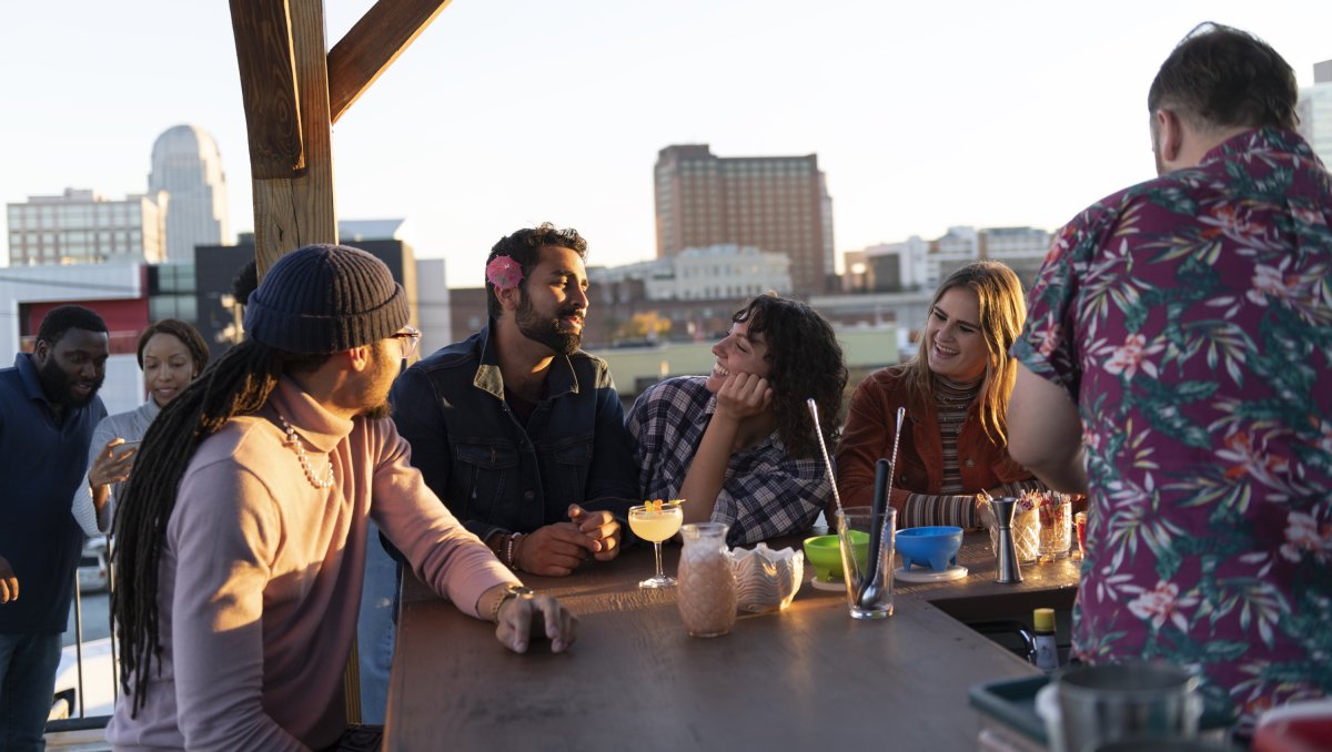 Friends enjoying colorful cocktails on rooftop bar with Winston-Salem skyline in back