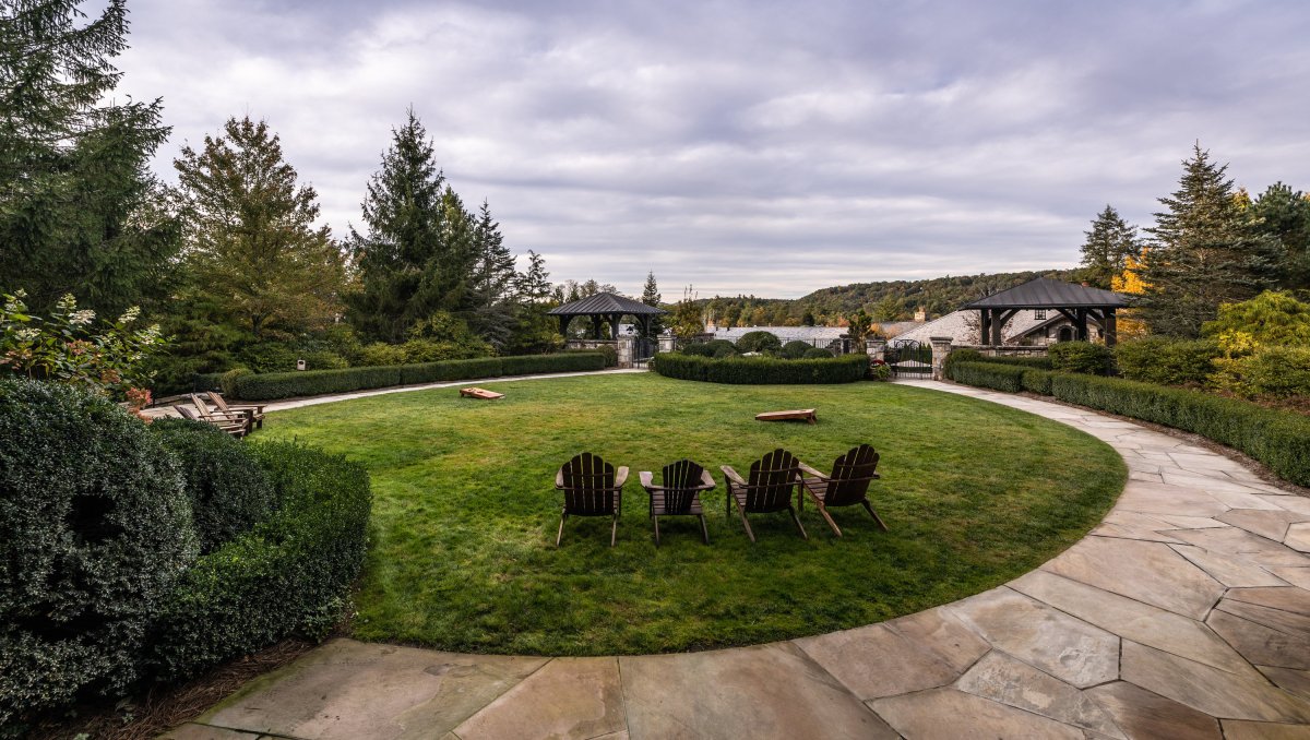 Four Adirondack chairs sitting on a green lawn looking out onto trees, lake and hills