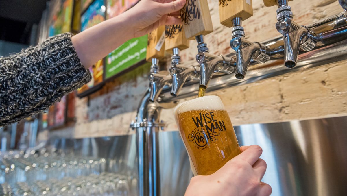 Hands pouring a pint of beer from a wall of taps