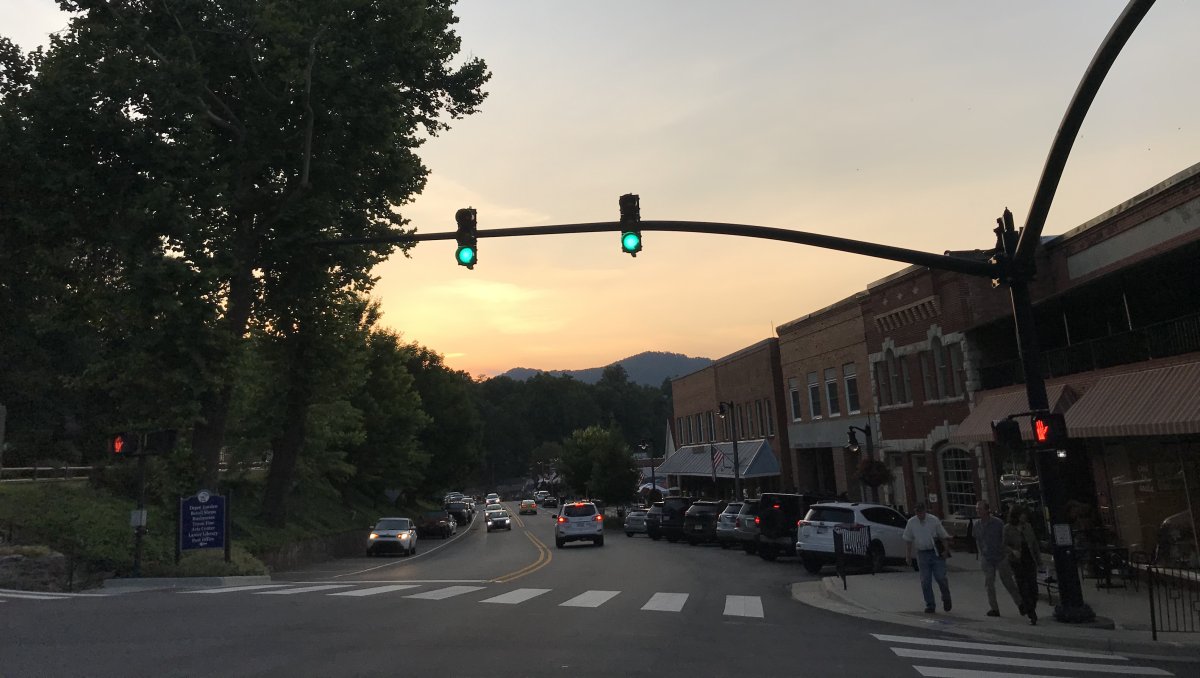 Small downtown Tryon at dusk with people walking on sidewalk, cars parked in downtown and mountains in distance