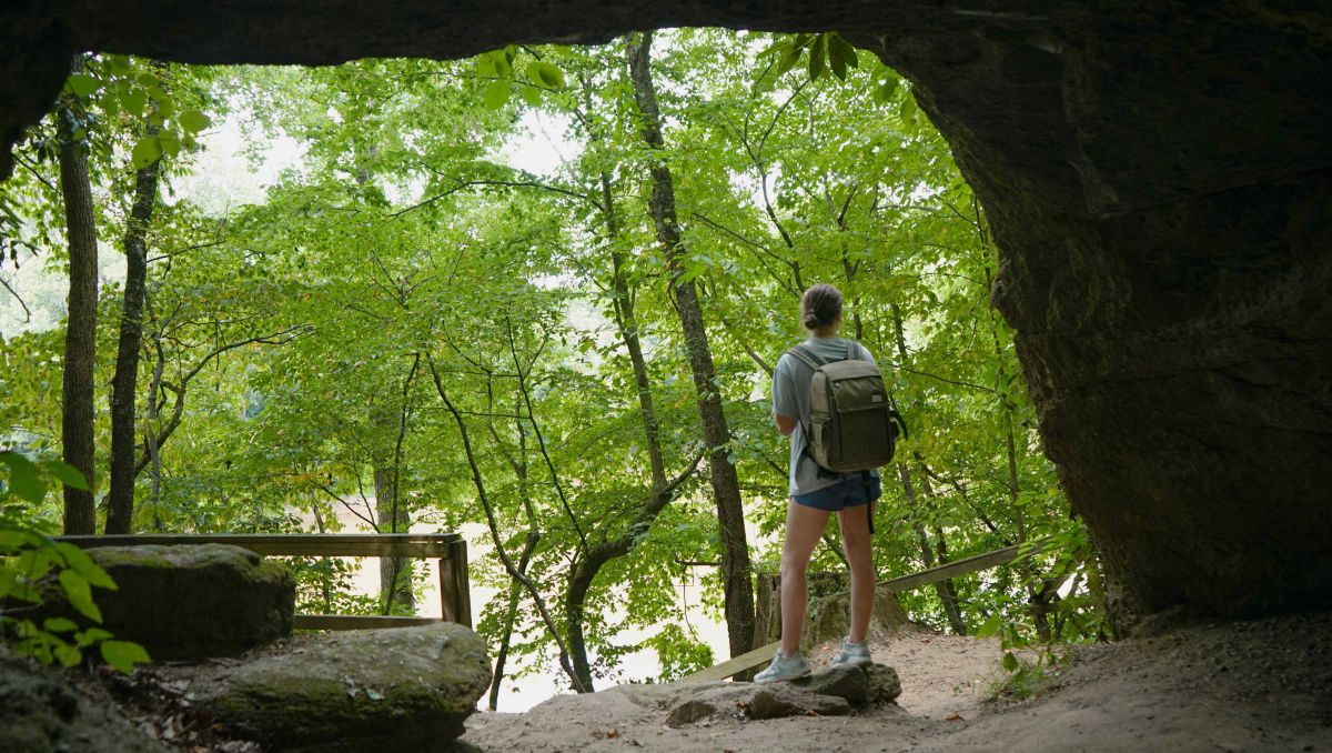 Woman standing outside of cave looking out into forest