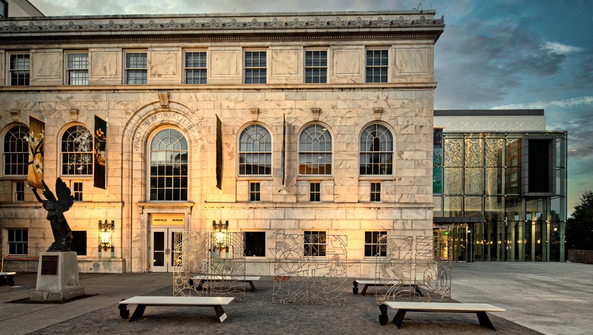 Exterior of Asheville Art Museum's beautiful building at dusk, with art in foreground.