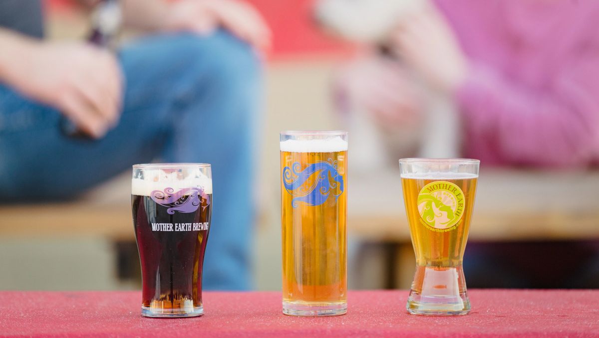 Three pints of beer lined up on table with people out of focus in background