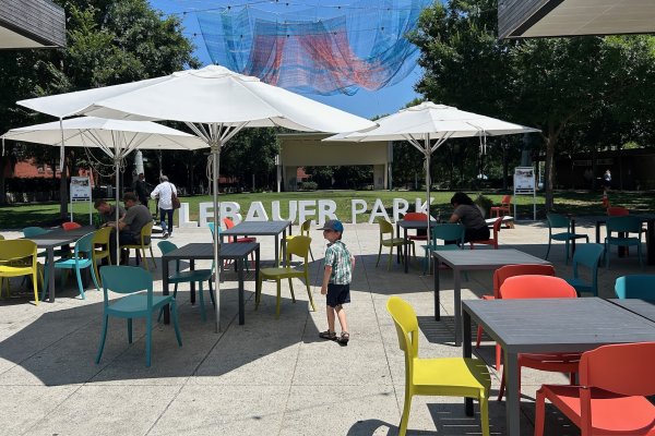 Boy walking through colorful tables and chairs in LeBauer Park under whimsical aerial art.