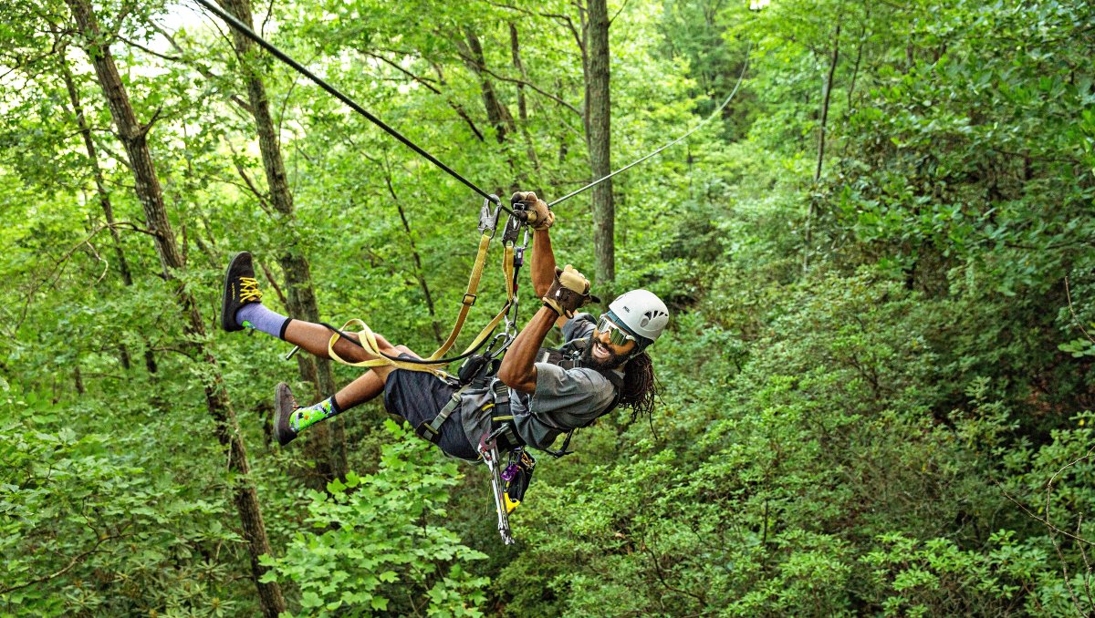 Person zip lining through green trees during daytime 