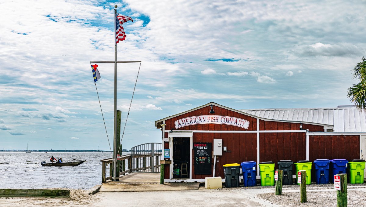 Exterior of front of bar next to water, with flag pole at entrance during daytime