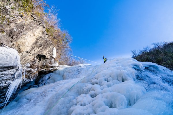 Man at top of frozen waterfall waving down to camera during daytime