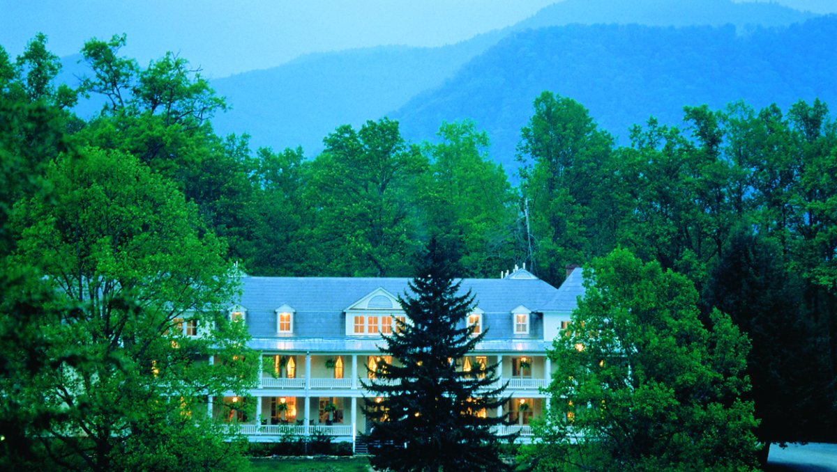 Exterior of white inn surrounded by green trees with Great Smoky Mountains in background