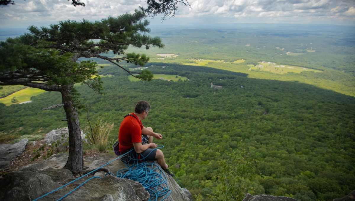 Man sitting on edge of cliff looking down to the valley during daytime
