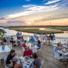 People dining on Jinks Creek Waterfront Grille patio with sunset in background