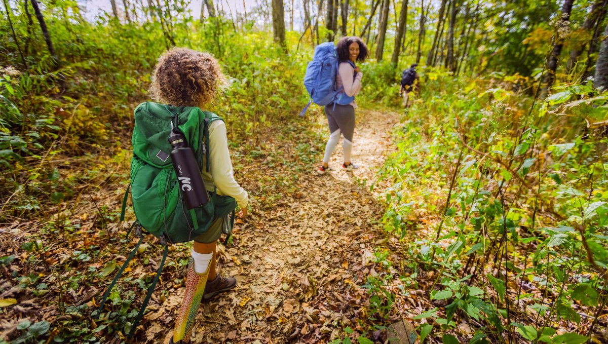 Family of three hiking Appalachian Trail while carrying big camping backpacks, surrounded by trees