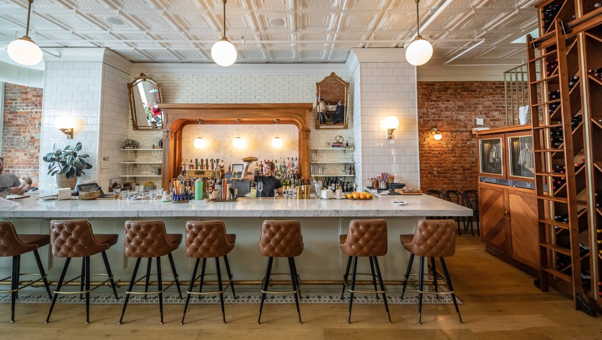 Bartender shaking drink behind empty bar in beautiful restaurant.