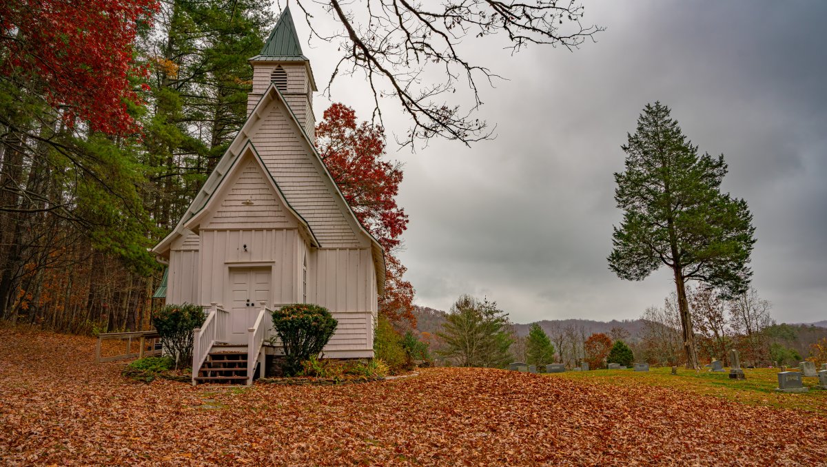 Old white church surrounded by brilliant fall foliage with mountains in background