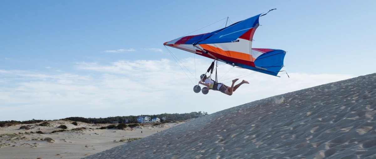 Person hang gliding over sand dunes during daytime