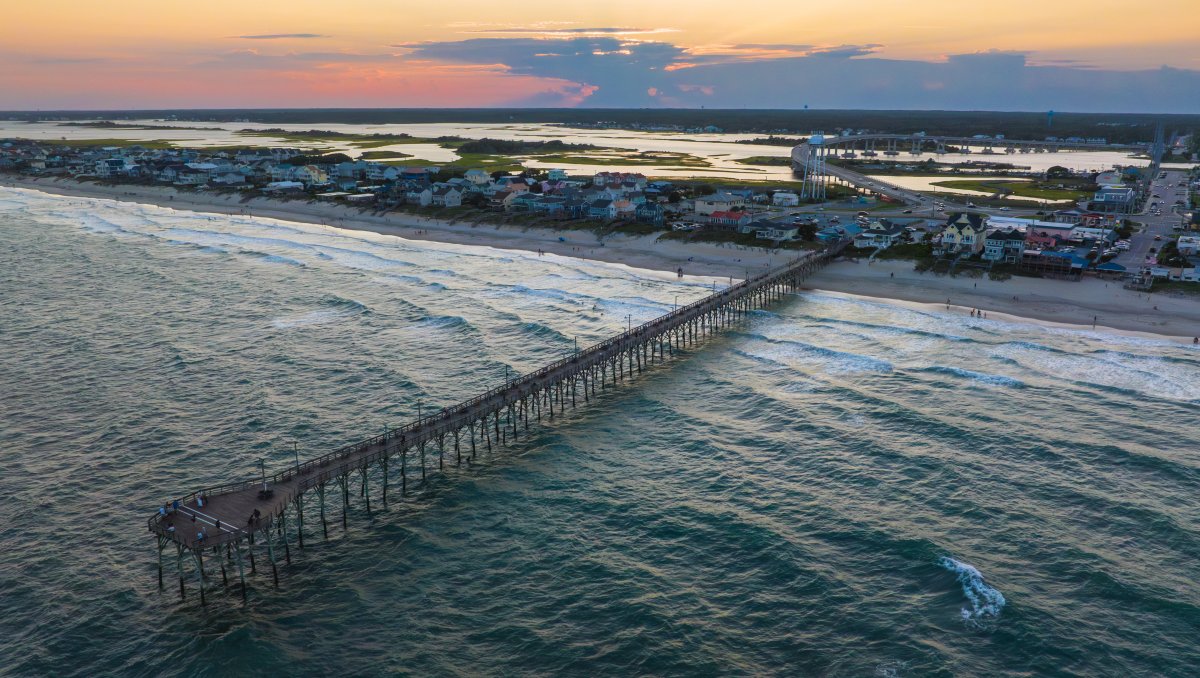 Aerial of Surf City Pier extending into water with land in background.