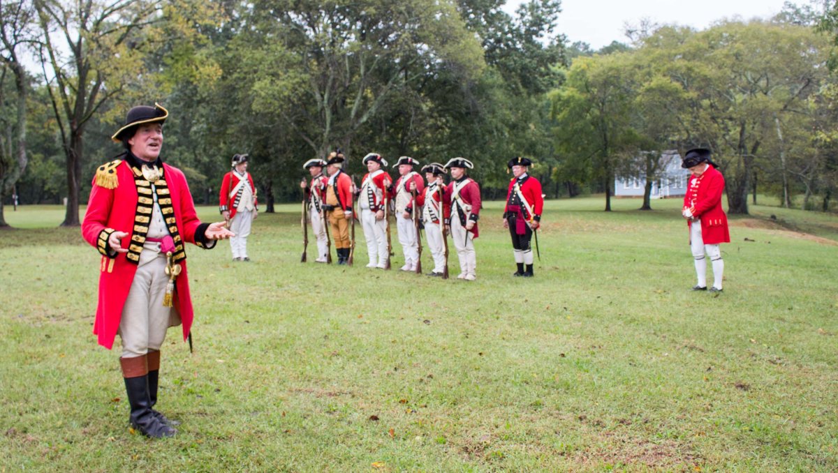 Revolutionary War re-enactors in red coats standing in open field with trees in background