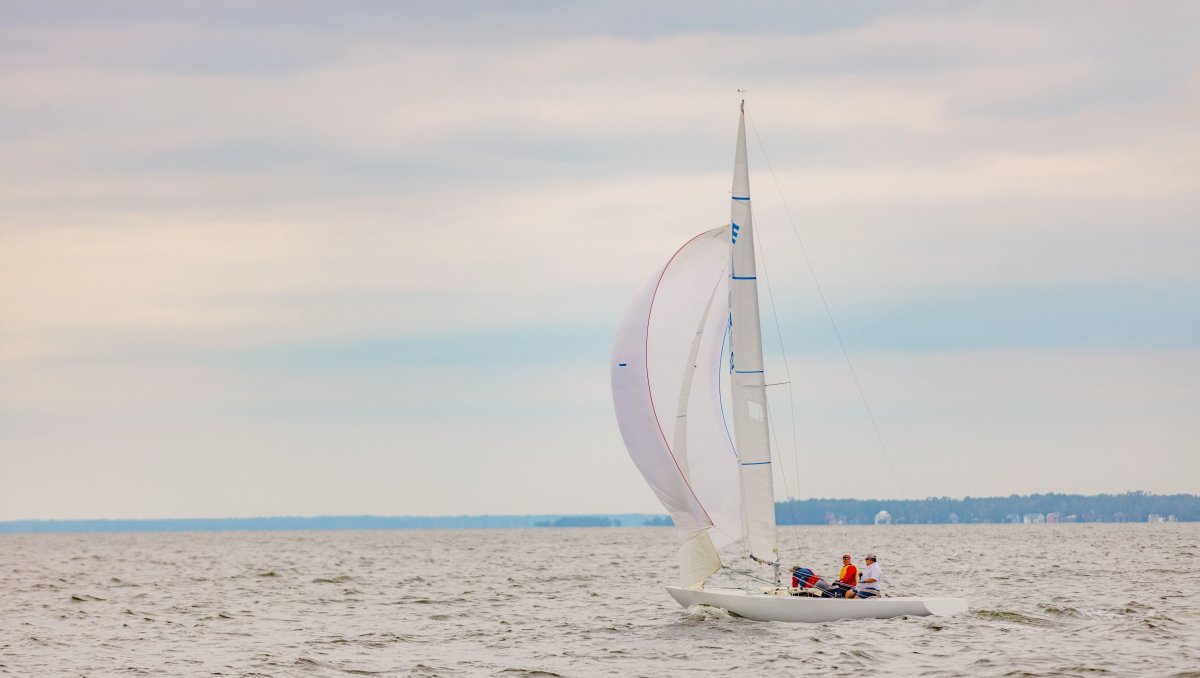 White sailboat on calm water on cloudy day