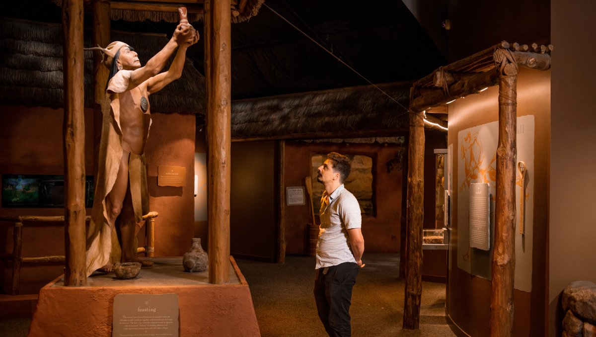 Man in Museum of the Cherokee People looking at Native American statue indoors