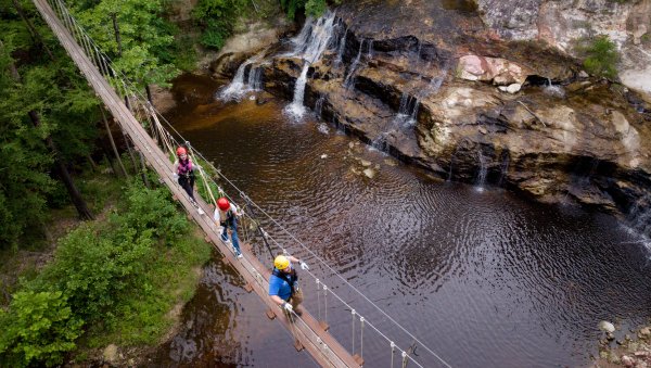 People walking on drawbridge over waterfalls and creek.