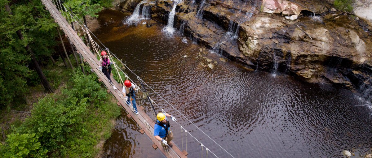 People walking on drawbridge over waterfalls and creek.