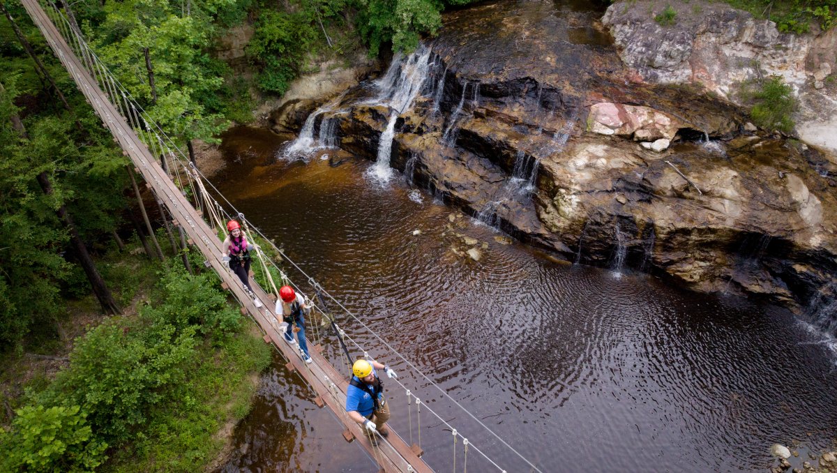 People walking on drawbridge over waterfalls and creek.