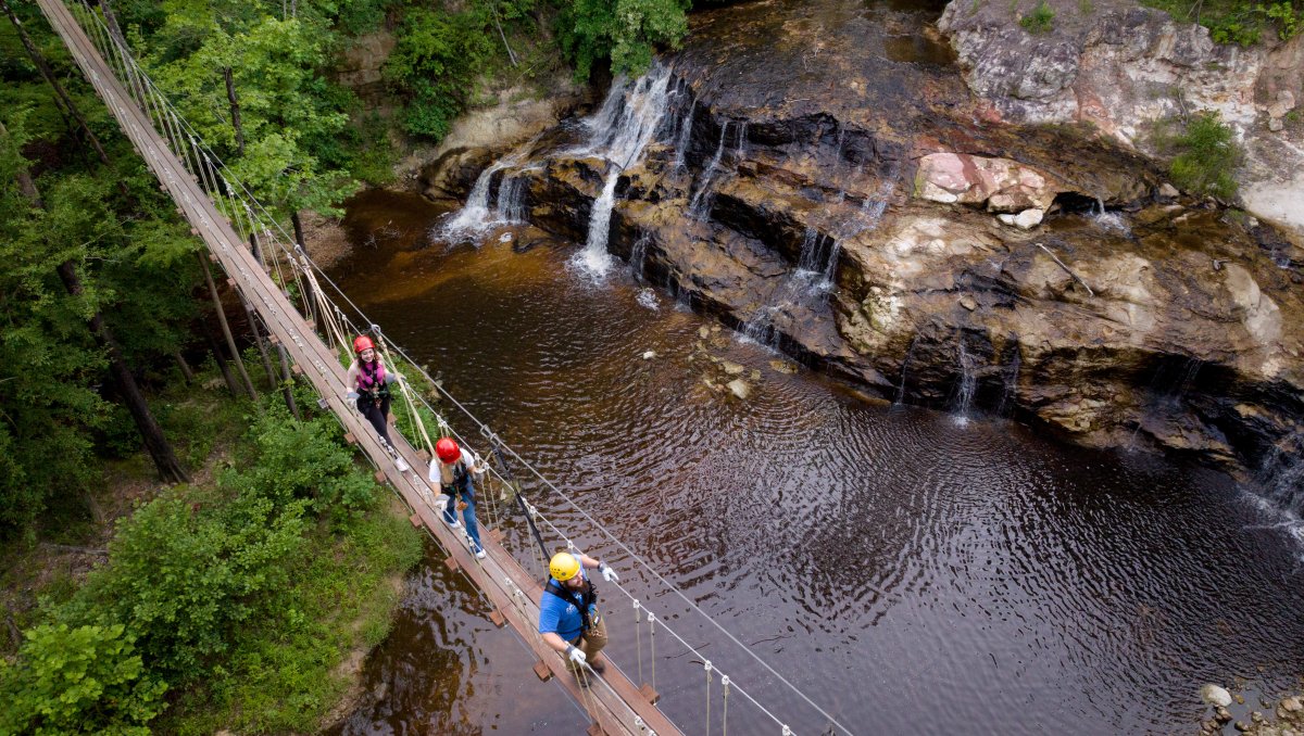 People walking on drawbridge over waterfalls and creek.