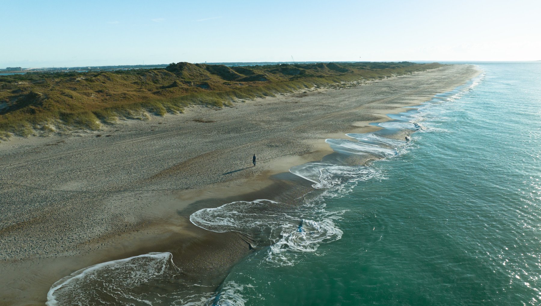 Aerial of beautiful, expansive Crystal Coast beach during summer daytime.