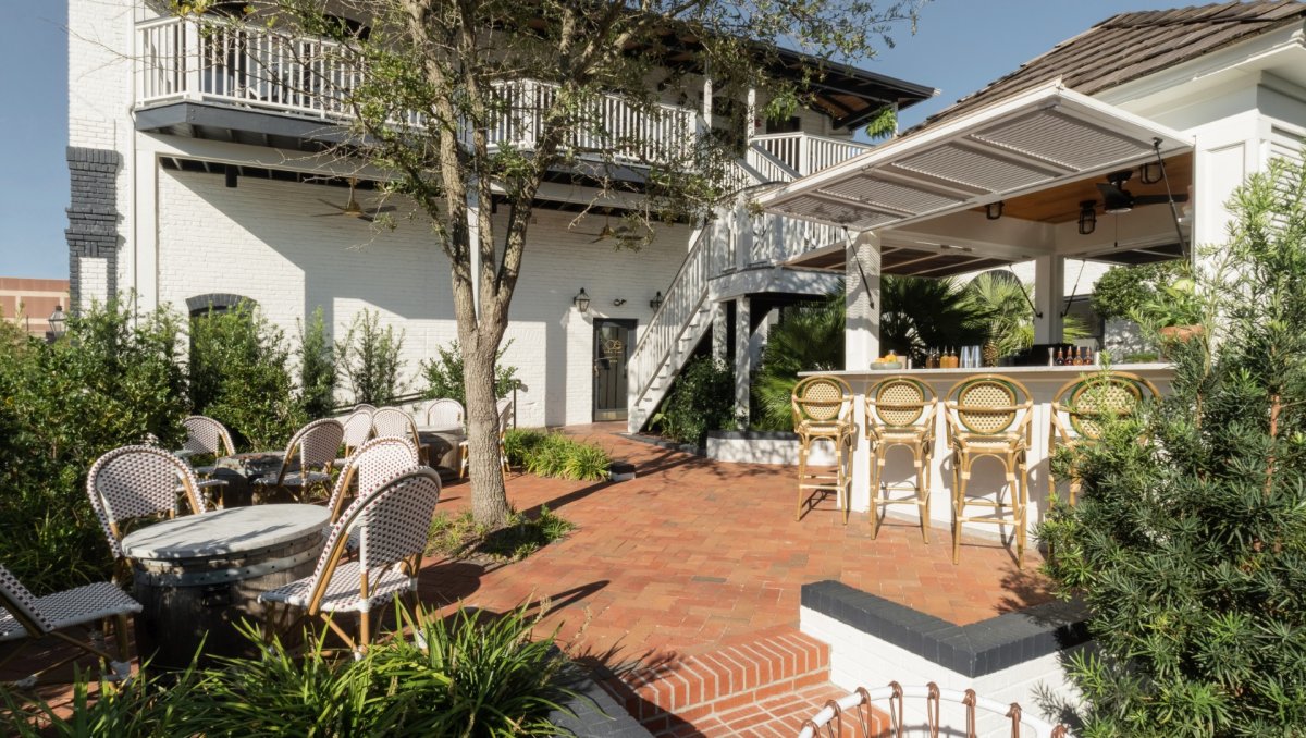 Exterior of hotel with outdoor bar and seating area, surrounded by green plants.