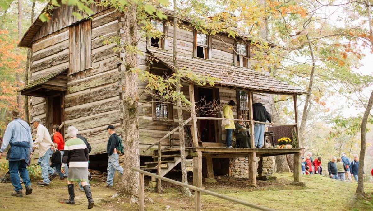 Groups of people exploring old log cabins surrounded by fall foliage