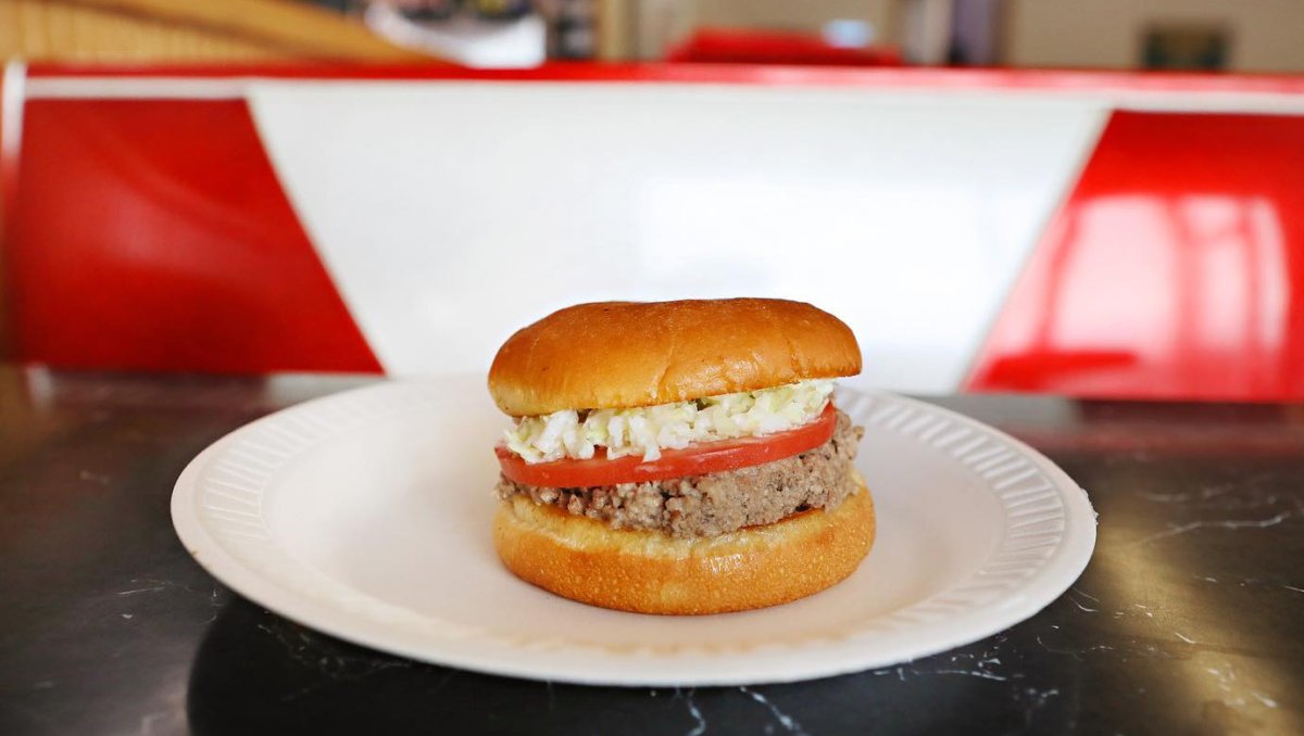 A delicious hamburger served on a white paper plate, showcasing its fresh ingredients and appetizing appearance.