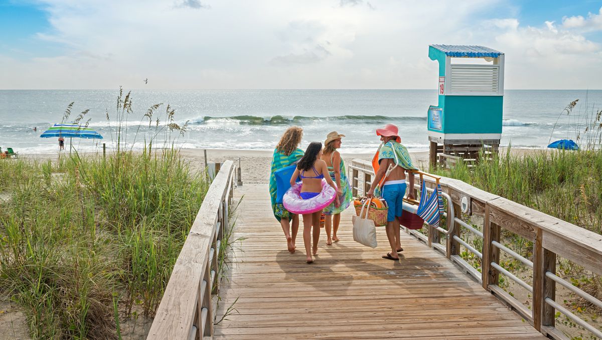 Family carrying beach supplies on beach access with ocean in background