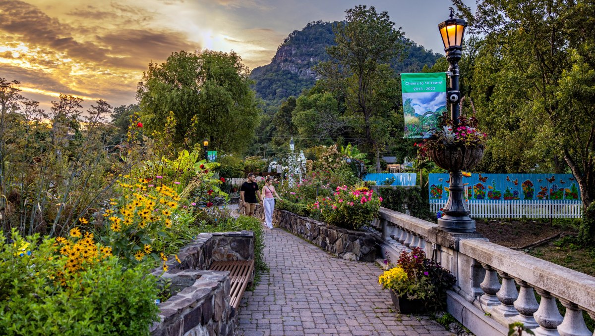 Couple admiring gardens on bridge, surrounded by plants and flowers with mountains in background as sun begins to set