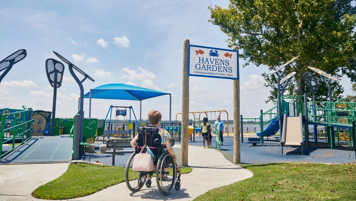 Person in wheelchair entering park with jungle gyms and other playground equipment