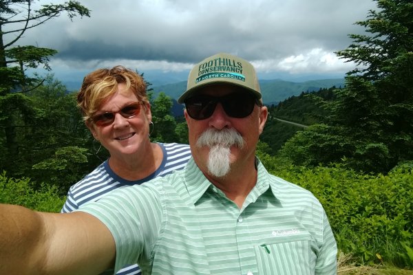 Husband and wife taking selfie on hiking trail with mountain views in background