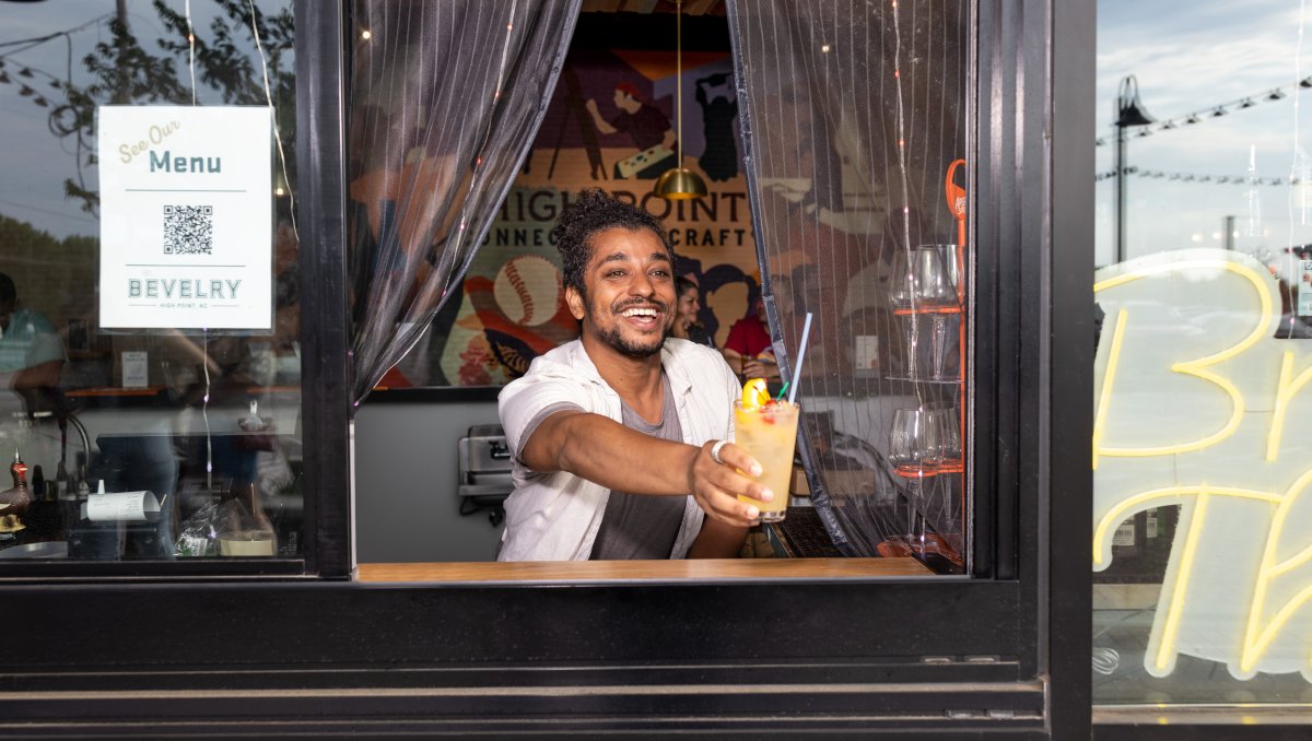 Bartender extending drink through order window at food hall.