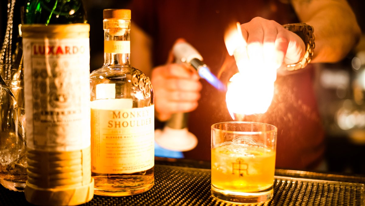 Bartender smoking a cocktail with fire with liquor bottle beside cocktail