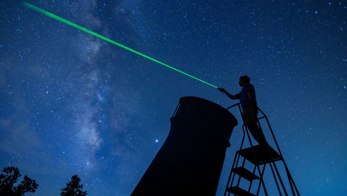 Person standing on ladder, pointing laser at night sky as they stargaze