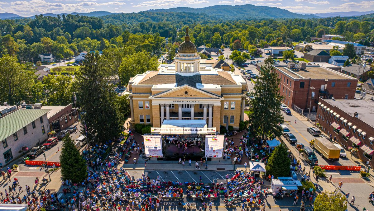 Shot of crowds at festival in front of Henderson County Courthouse with green mountains in background during daytime