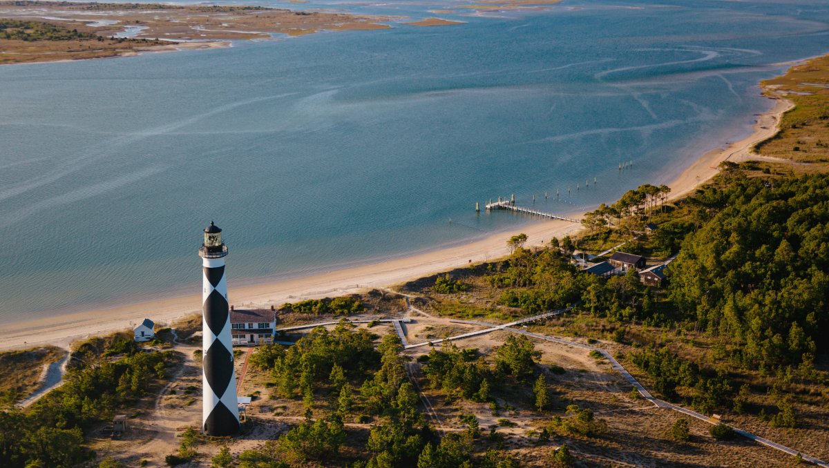 Aerial view of Cape Lookout Lighthouse in foreground with land and water in background during daytime