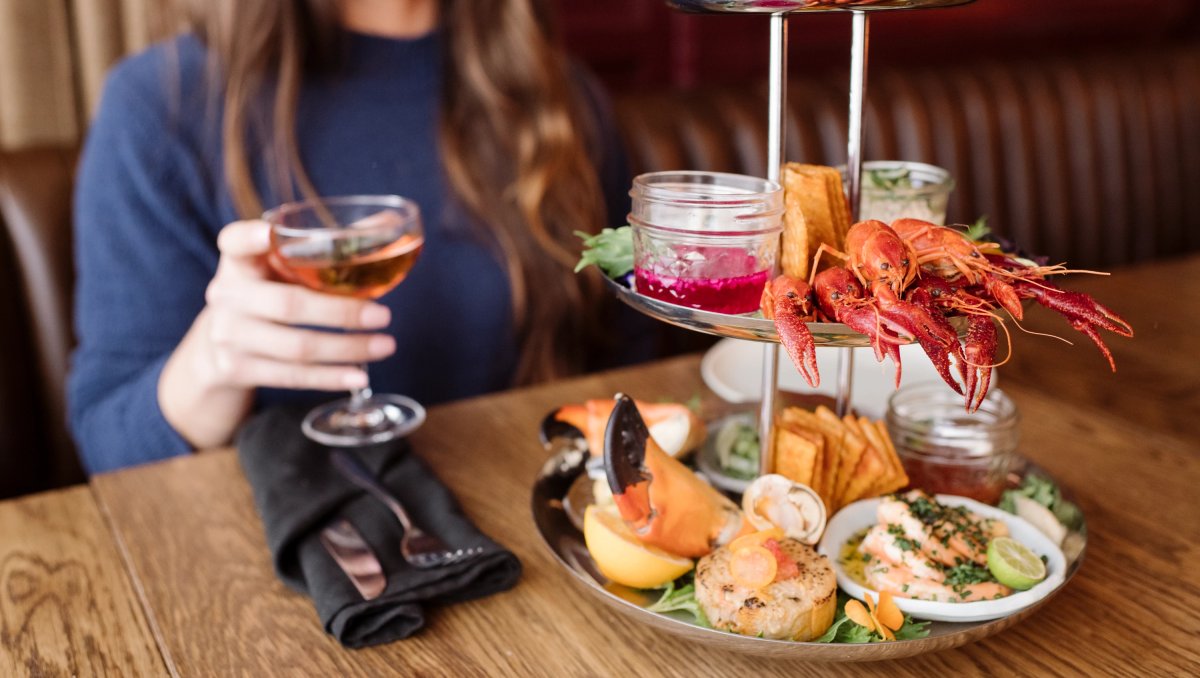 Woman holding cocktail sitting at table with seafood tower in front of her