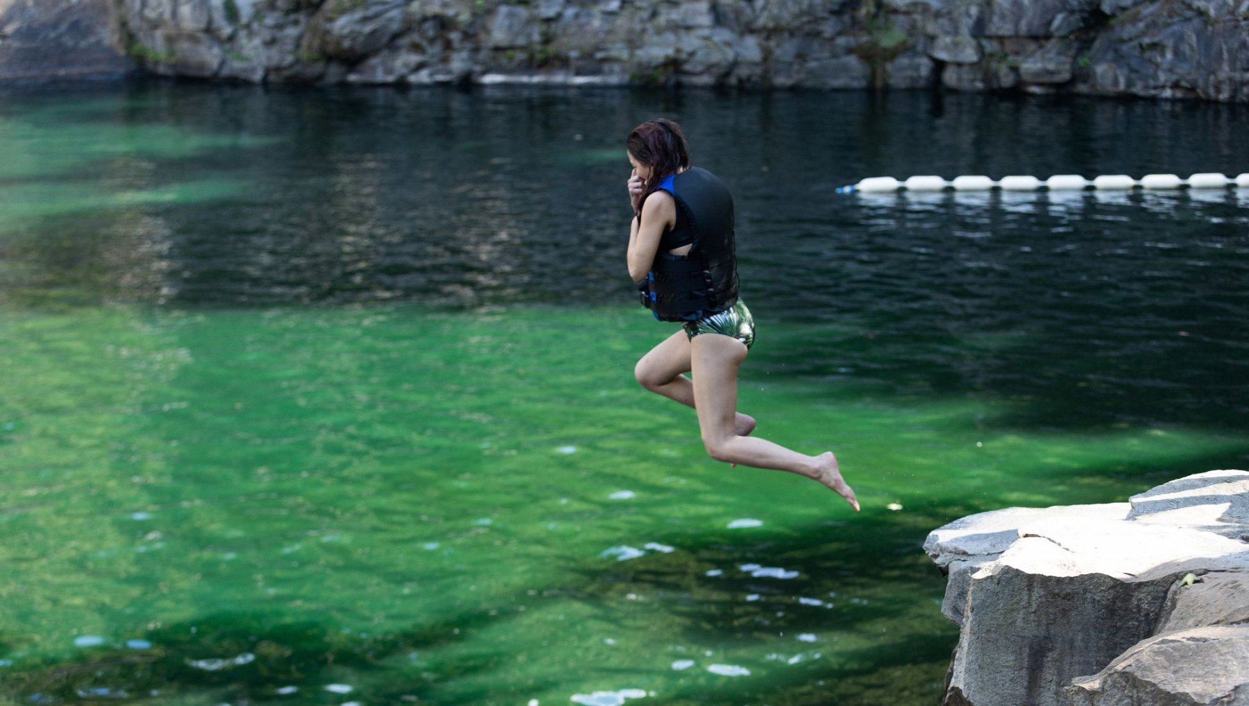 Girl jumping off stone into quarry with stone wall in background.