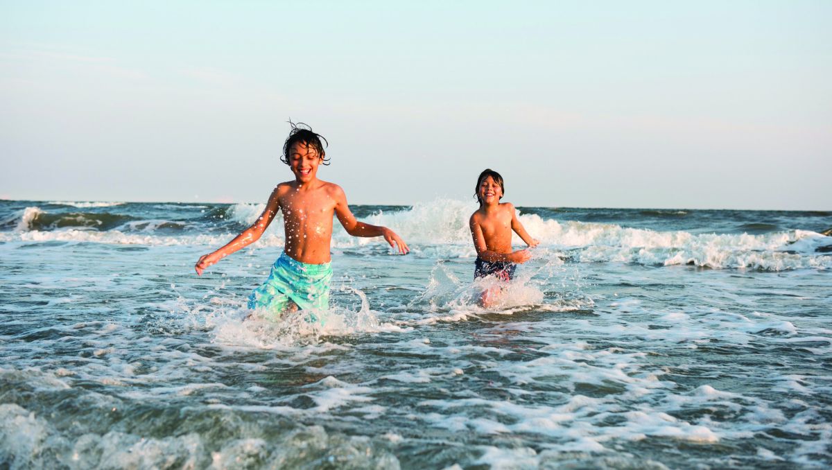 Two smiling boys splashing through waves in Ocean Isle Beach in the Brunswick Islands