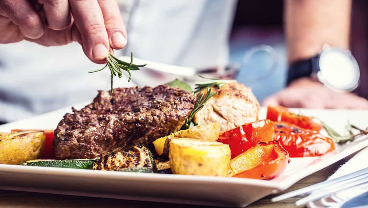 Close-up of chef placing garnish on top of steak and veggie dinner