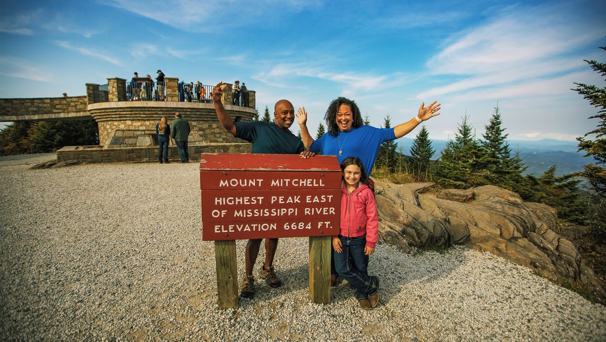 Family posing next to Mount Mitchell sign at the peak of the mountain
