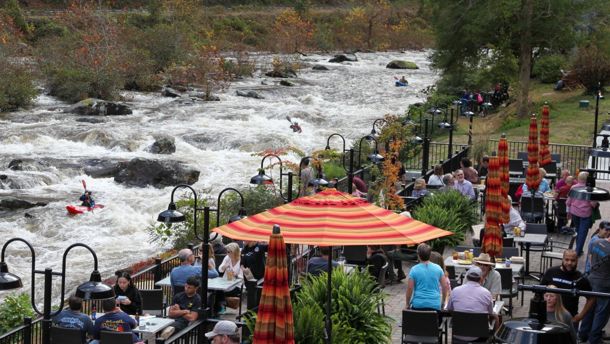 Tables of diners on patio at Historic Tapoco Lodge with raging river and kayakers to the left.