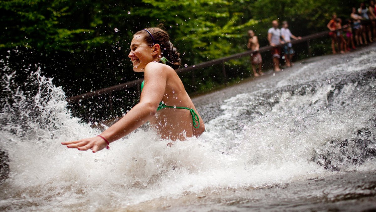 Girl sliding down rock and plunging into natural pool with spectators in background
