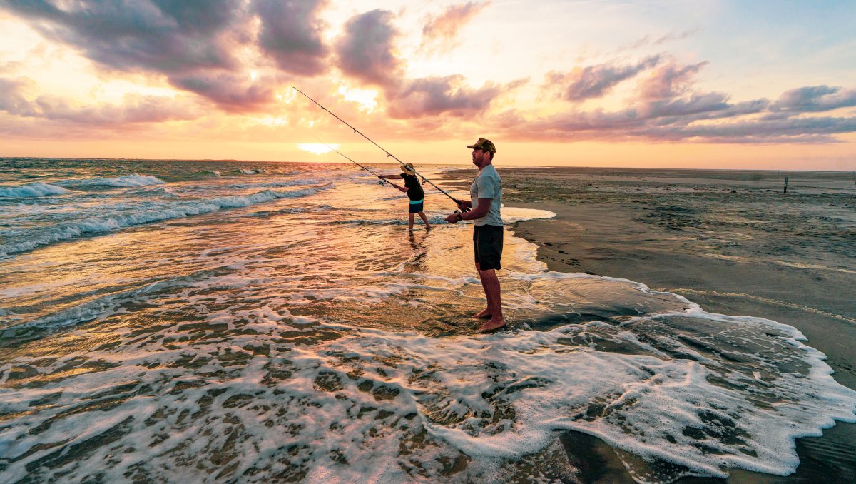 Two people surf cast fishing at sunset in Ocracoke, NC.