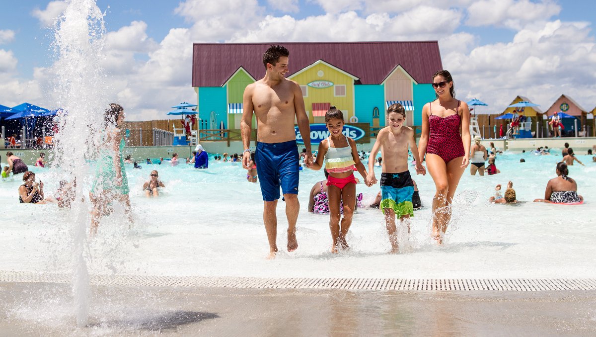 Family of four holding hands walking out of wave pool at Carolina Harbor at Carowinds.